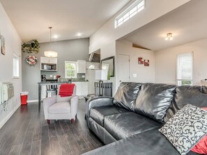 A modern living room with a leather sofa, a white armchair, and a dining area with a kitchen in the background.