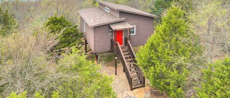 A cabin with a red door, a wooden staircase, and a view of a body of water.