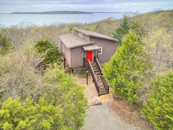 A cabin with a red door, a wooden staircase, and a view of a body of water.