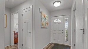 A hallway with white doors, a wooden floor, a doormat, and a wall-mounted air conditioning unit. - Stylish Two-Story Getaway on Keizer's Quiet Outskirts (Keizer)