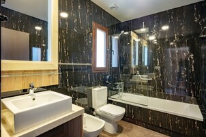 Un baño moderno con un lavamanos grande, inodoro, bidé y zona de ducha con mampara de vidrio.