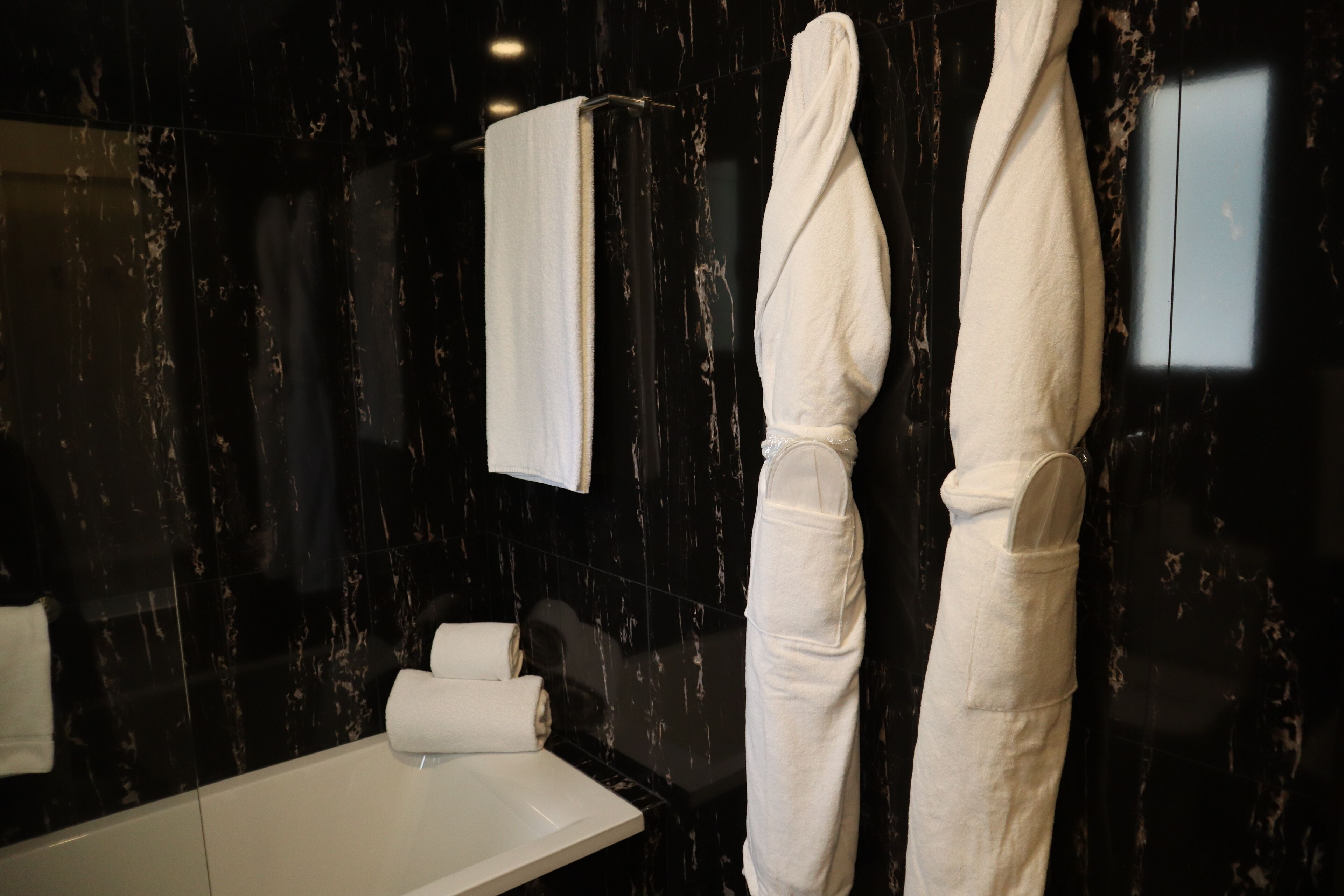 A bathroom with a black marble wall, a white sink, and two white towels hanging on hooks.