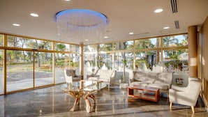 Een ruime lobby met een moderne kroonluchter, comfortabele zithoeken en grote ramen met uitzicht op het omliggende landschap.