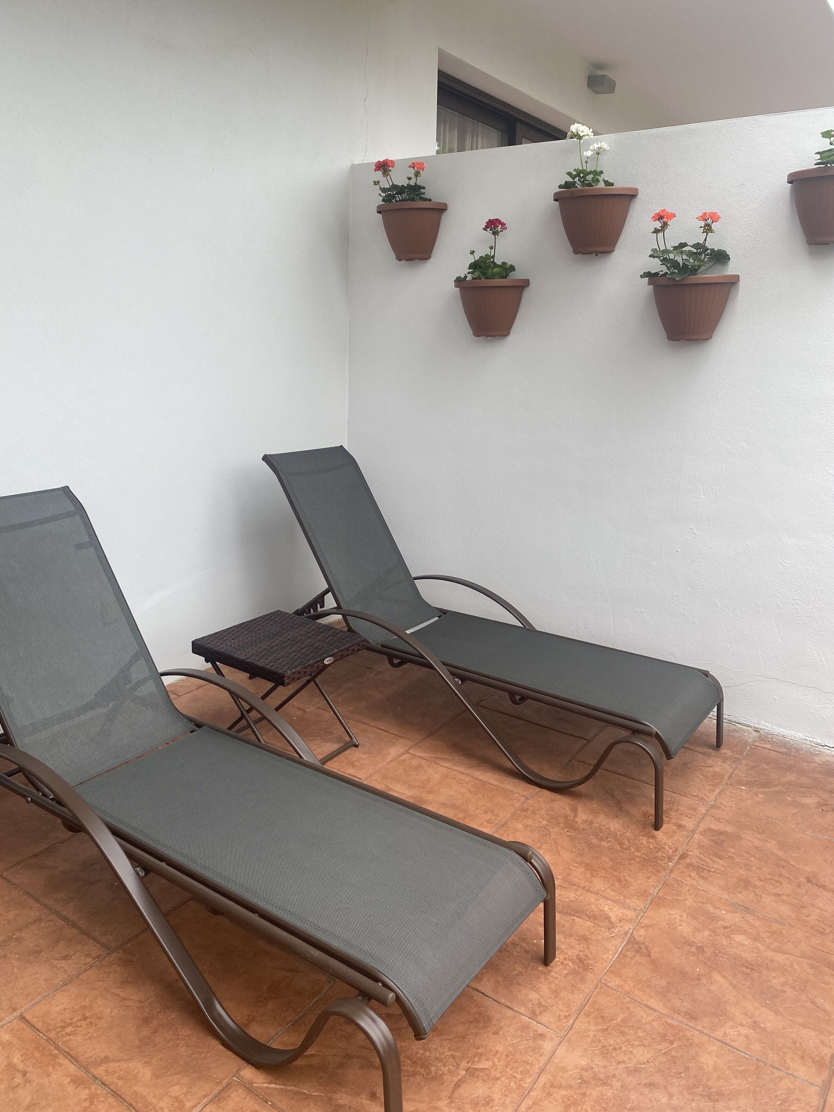 Dos sillones reclinables con estructura metálica y respaldos de malla, ubicados en un patio empedrado con baldosas de terracota.