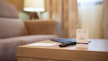 A hotel room with a wooden nightstand, a remote control, and a welcome card.