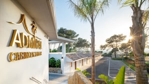Het uiterlijk van Adriamira Casino & Lodge, met een verharde oprit, een stenen muur en palmbomen.