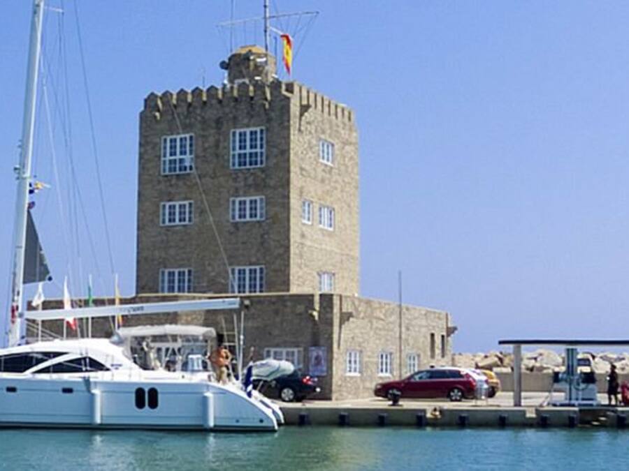 Un puerto deportivo con un yate blanco amarrado cerca de un edificio de piedra con varias ventanas y una bandera.