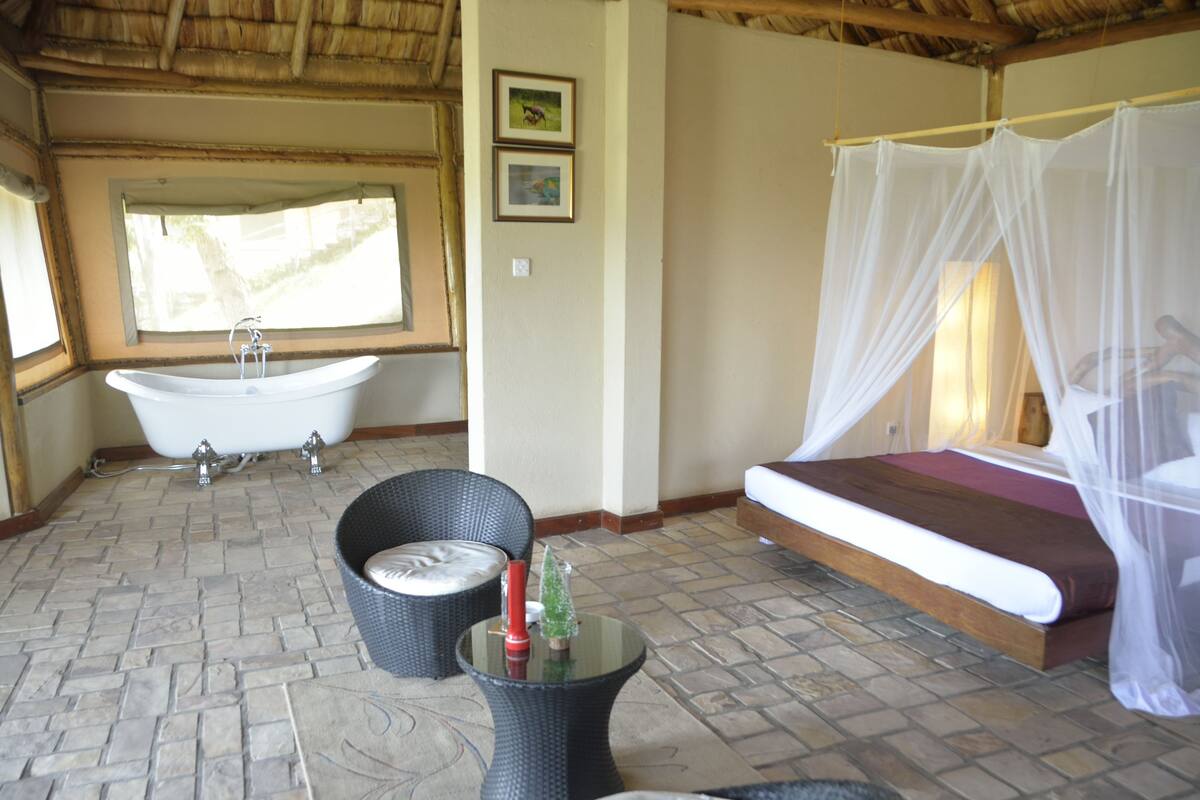 A bathroom with a bathtub, a bed with a canopy, wicker furniture, and a small table with decorative items.