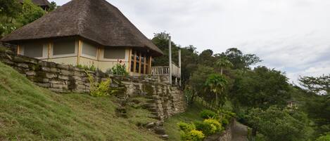 A thatched-roof house with a stone retaining wall and a stone pathway.
