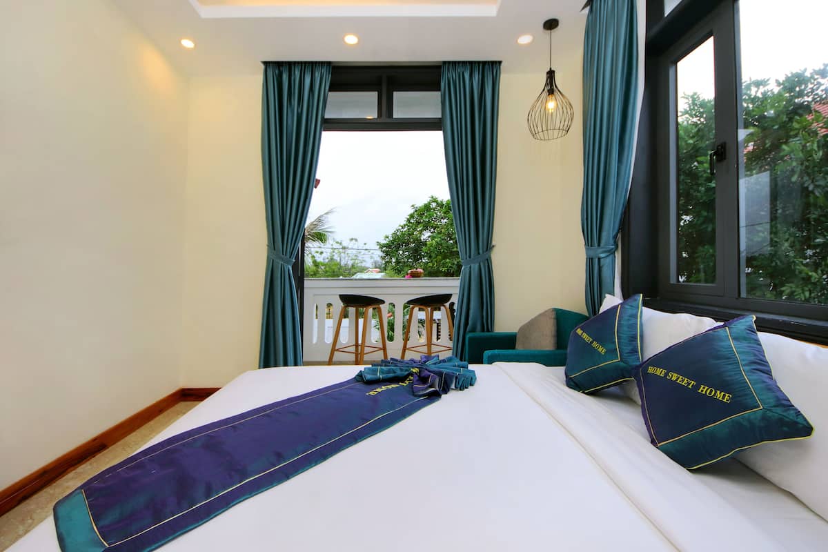 A hotel room with a bed, two chairs, a window with curtains, and a view of greenery outside.