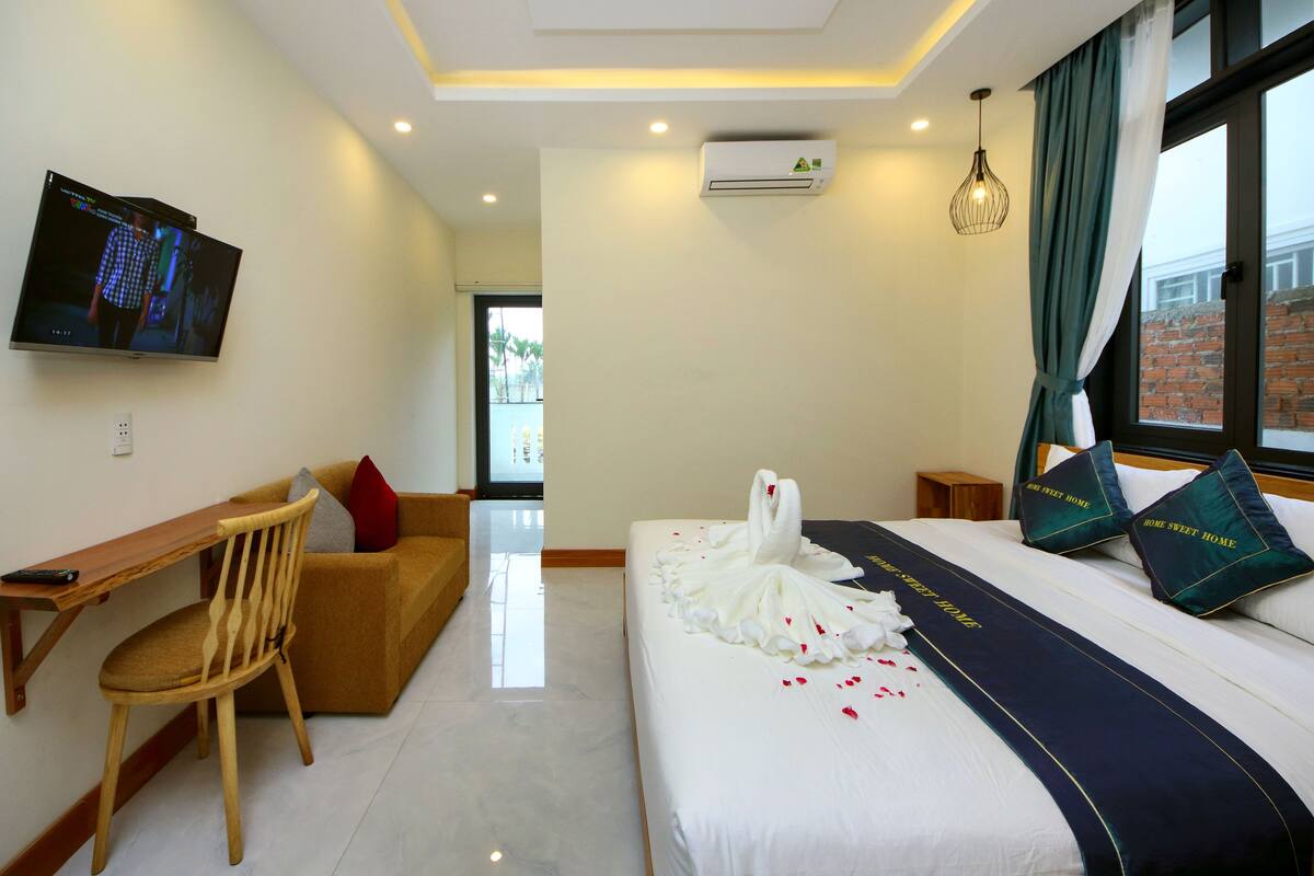A hotel room with a bed, a desk, a chair, a TV, and a window with curtains.