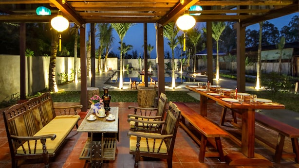 An outdoor patio with wooden furniture, including benches and a table, under a wooden pergola with hanging lights. - Home Sweet Home Villa (Da Nang)