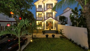 A two-story house with a balcony, a well-lit entrance, and a car parked in the driveway. - Home Sweet Home Villa (Da Nang)