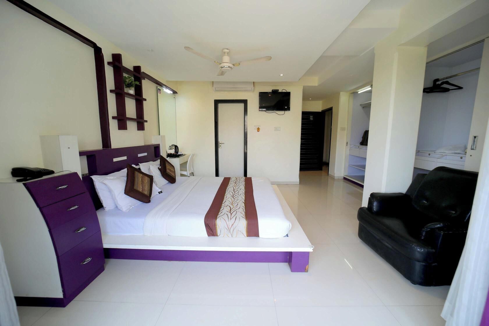 A hotel room with a bed, a desk, a chair, a wardrobe, and a TV.