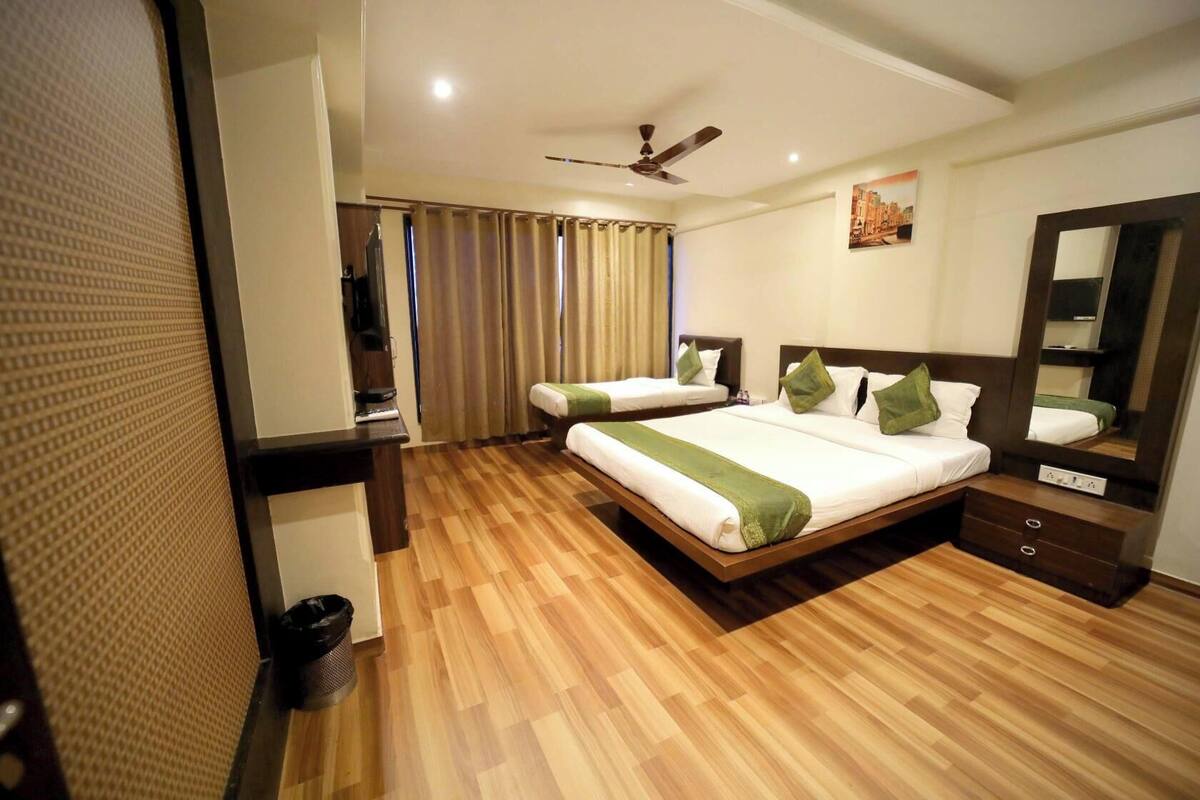 A hotel room with two single beds, a large mirror, a ceiling fan, and a wooden floor.
