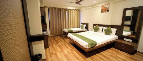 A hotel room with two single beds, a large mirror, a ceiling fan, and a wooden floor.