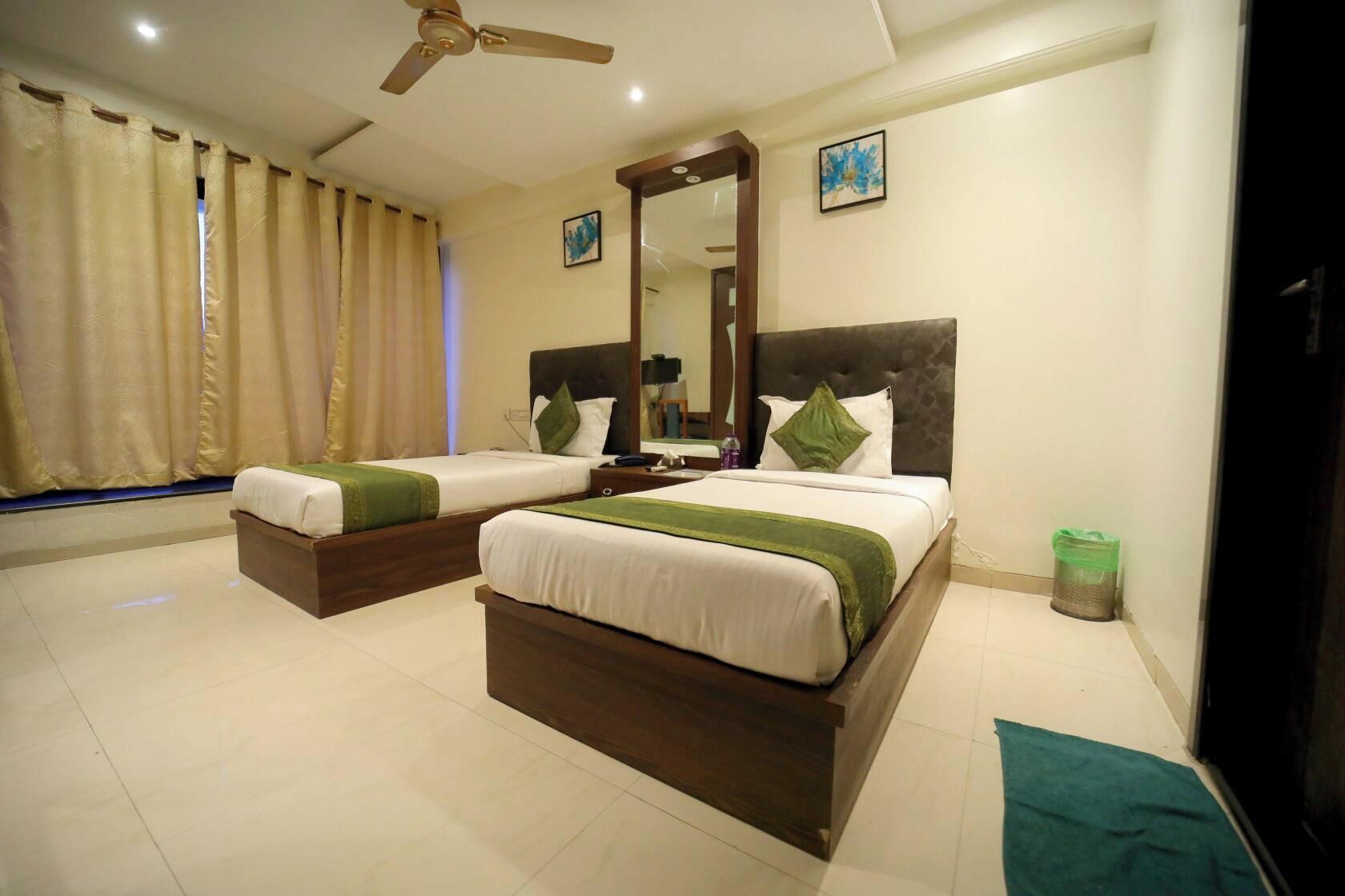 A hotel room with two beds, a ceiling fan, a large mirror, and a trash bin.
