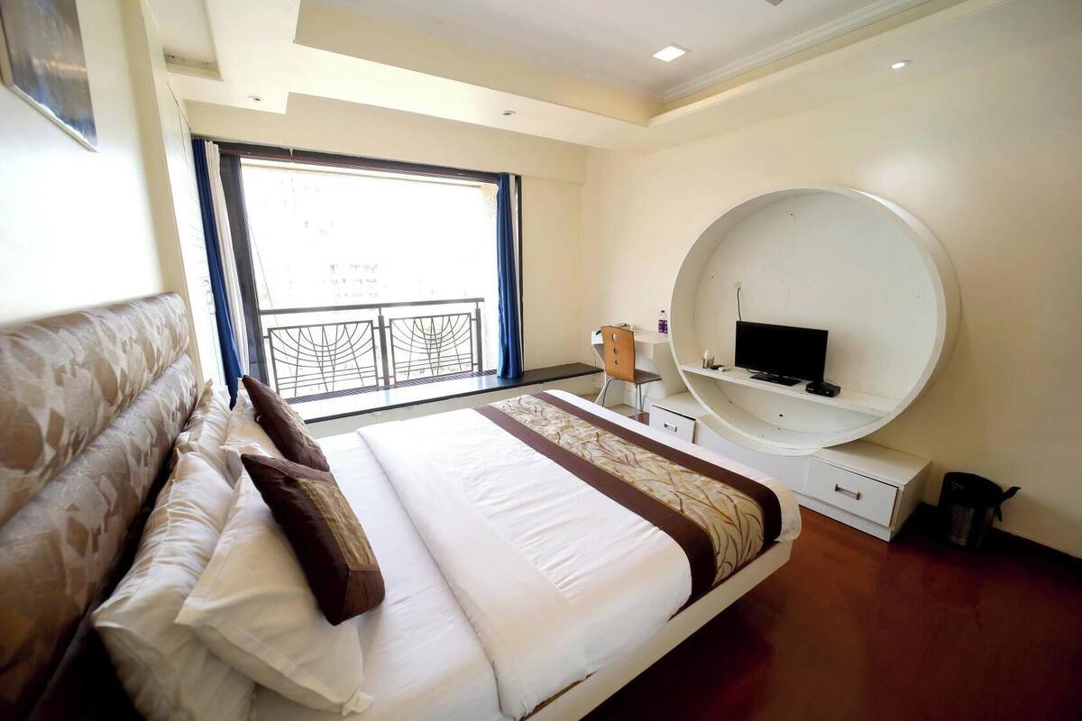 A hotel room with a large bed, a round mirror, a desk, and a balcony with a railing.