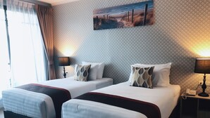 Een hotelkamer met twee bedden, een schilderij van een strandgezicht, een telefoon en een lamp op het nachtkastje.