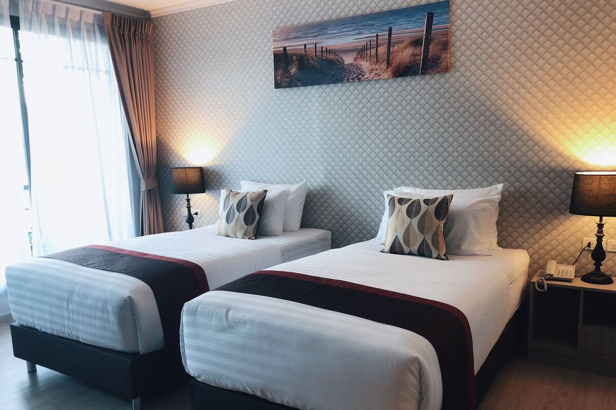 Een hotelkamer met twee bedden, een schilderij van een strandgezicht, een telefoon en een lamp op het nachtkastje.
