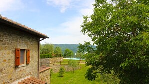 A stone building with a balcony, a lawn, and a view of a lake. - A very old small stone hamlet set in a panoramic position a few km from the city of Arezzo. Endowed (Palazzo del Pero)