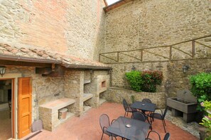 A stone building with a tiled roof, outdoor seating area with tables and chairs, and a stone fireplace.