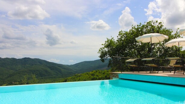 A clear blue infinity pool with a view of green hills and a cloudy sky. - A very old small stone hamlet set in a panoramic position a few km from the city of Arezzo. Endowed (Palazzo del Pero)