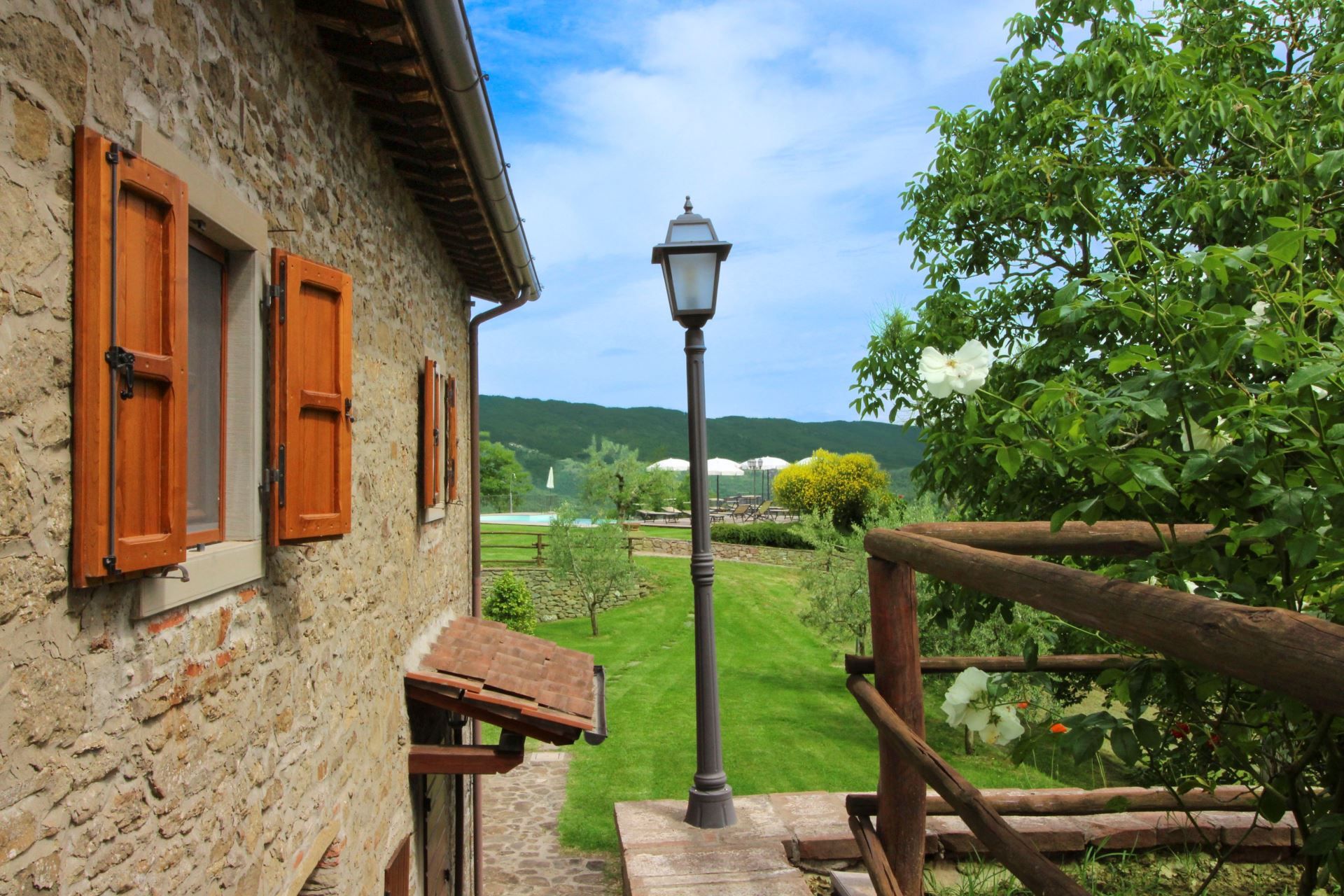 Un edificio de piedra con contraventanas de madera, un farol y una valla de madera que da a un paisaje verde.