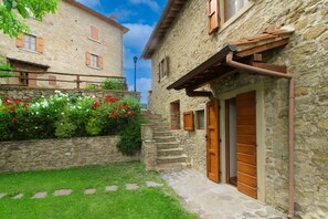 A stone building with a wooden door and steps leading to a garden with red and white flowers.