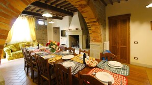 A dining area with a wooden table set for four, a sofa, and a fireplace in the background. - A very old small stone hamlet set in a panoramic position a few km from the city of Arezzo. Endowed (Palazzo del Pero)