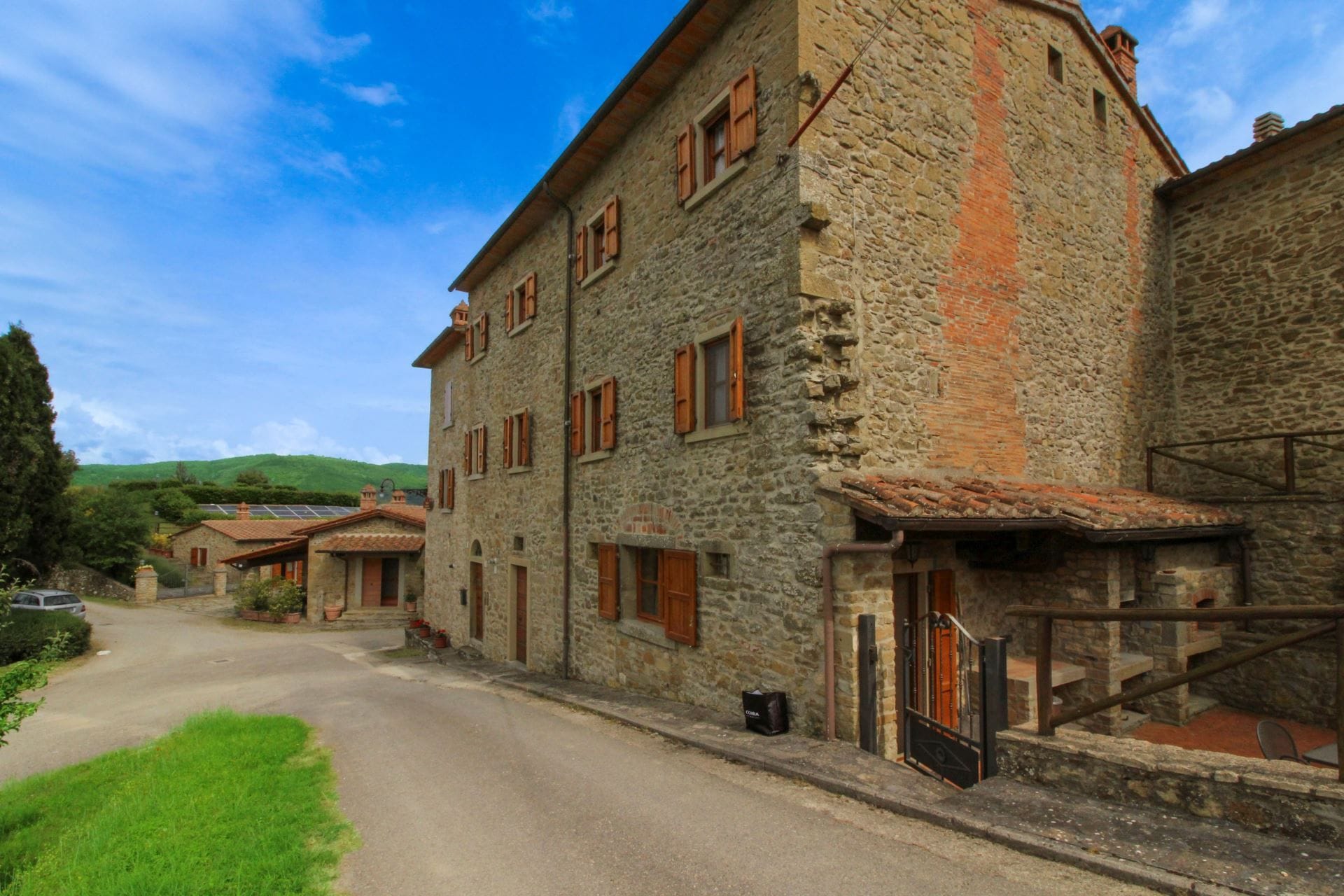 A stone building with multiple windows and a door, a paved road in front, and a green landscape in the background.