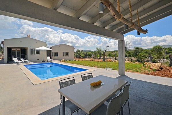 A covered outdoor area with a pool, lounge chairs, and a table with fruit.