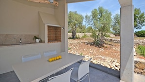 An outdoor kitchen with a table, chairs, a brick oven, and a view of a rocky landscape with trees.