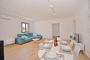 A modern living room with a blue sofa, dining table set for four, and a TV on a stand.