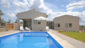 A modern house with a swimming pool, two lounge chairs, and a patio umbrella.