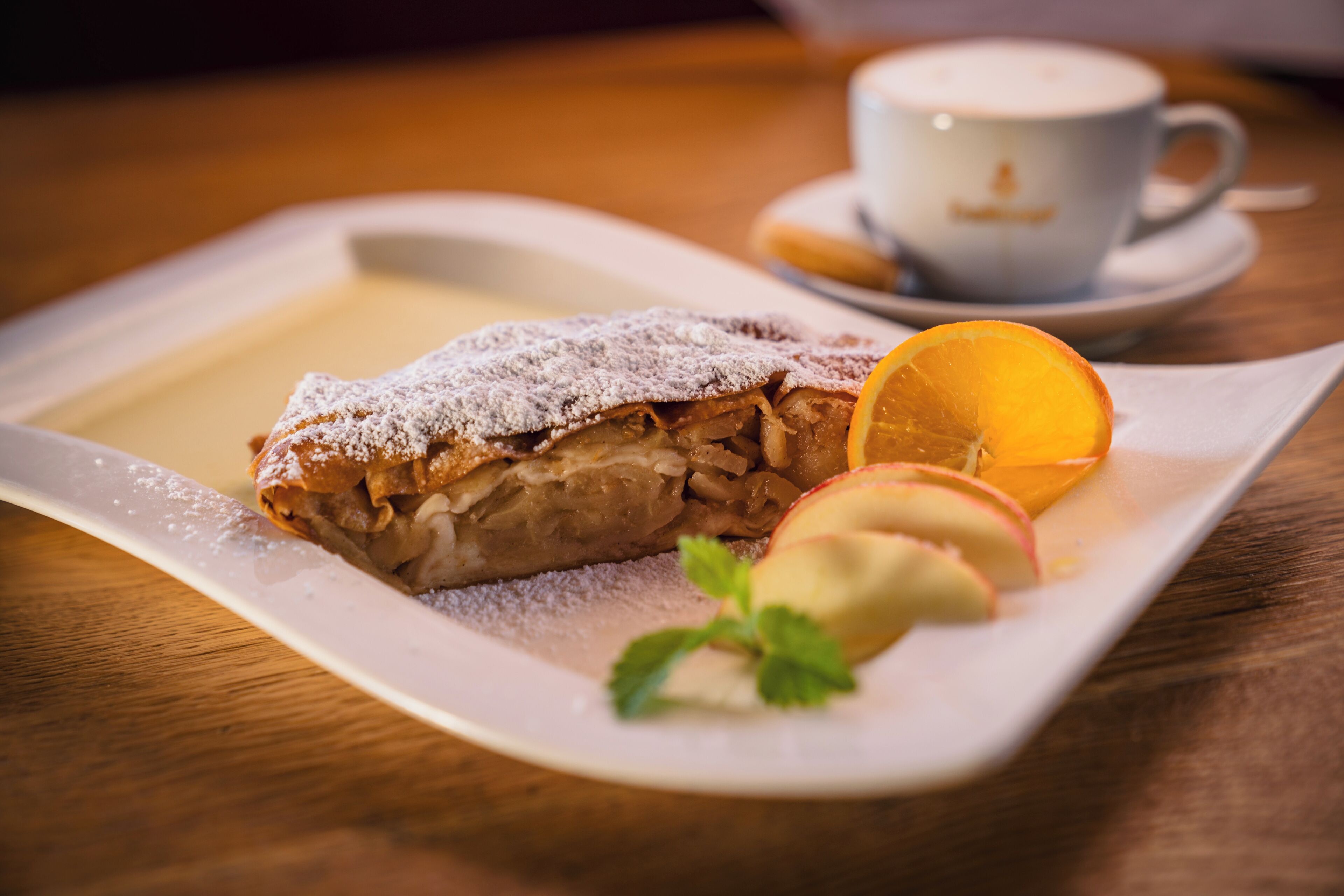 A dessert plate with a pastry, a slice of orange, and a mint garnish on a white plate.