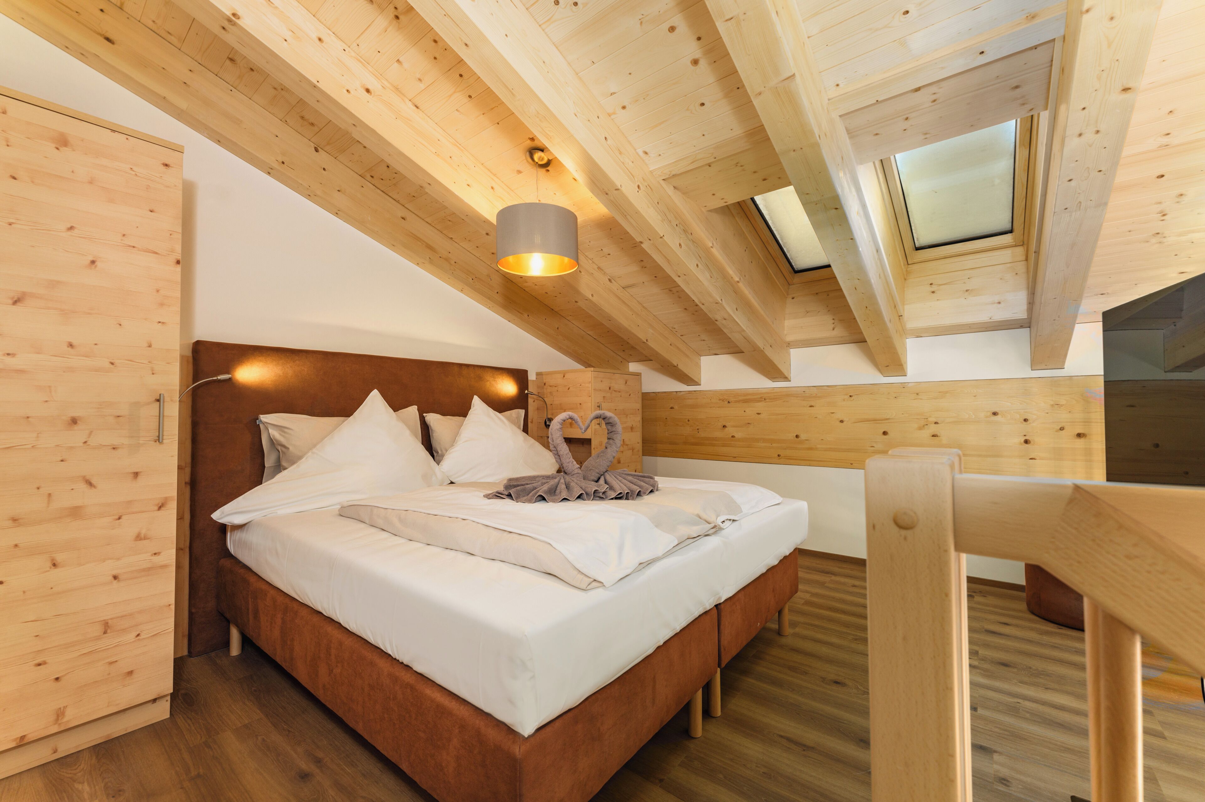 Una habitación con paneles de madera, una cama, cabecera, tragaluz y una silla de madera.