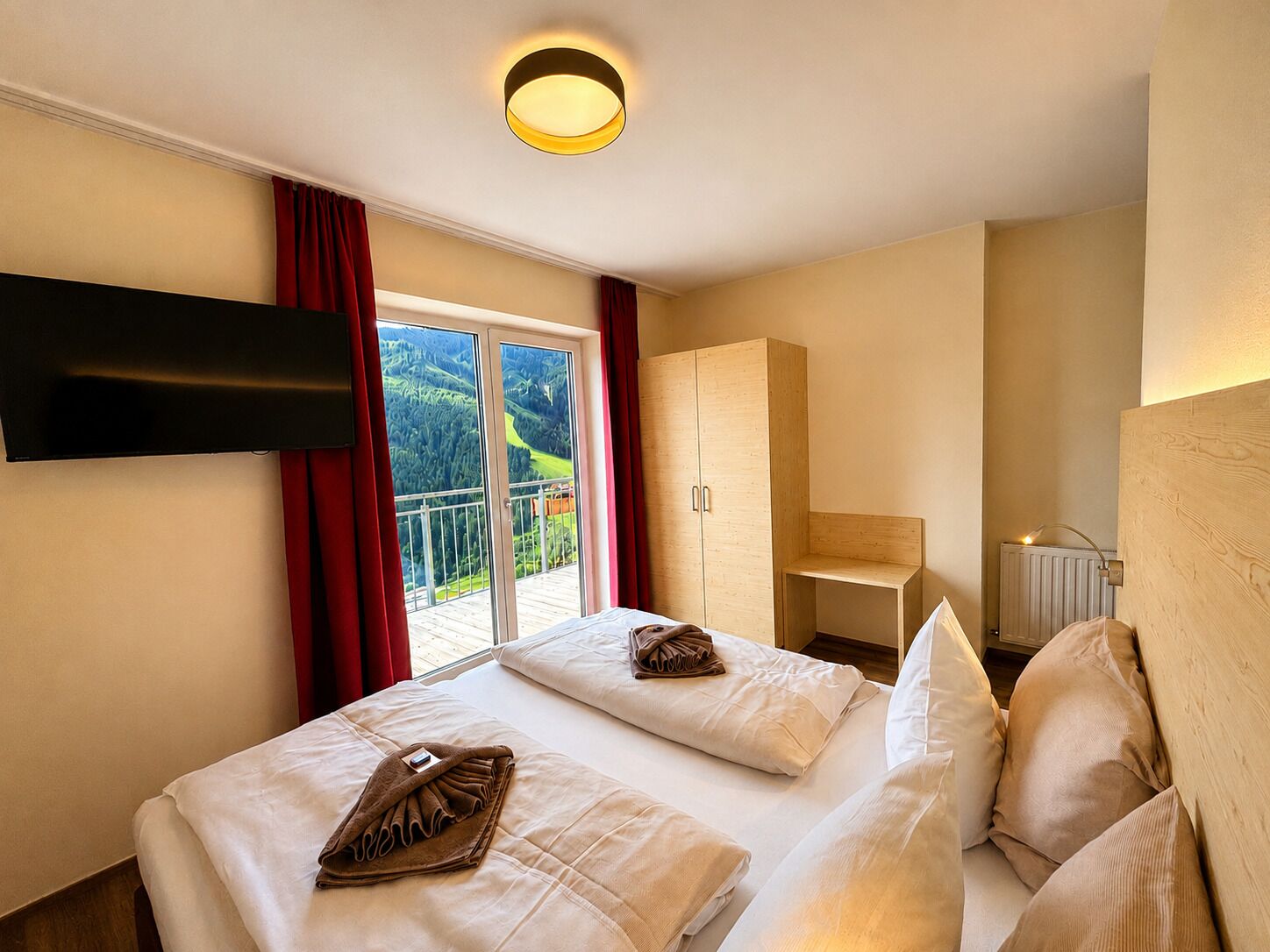 Une chambre d’hôtel équipée d’un lit, d’une télévision, d’une armoire, d’une petite table et offrant une vue sur un paysage montagneux.