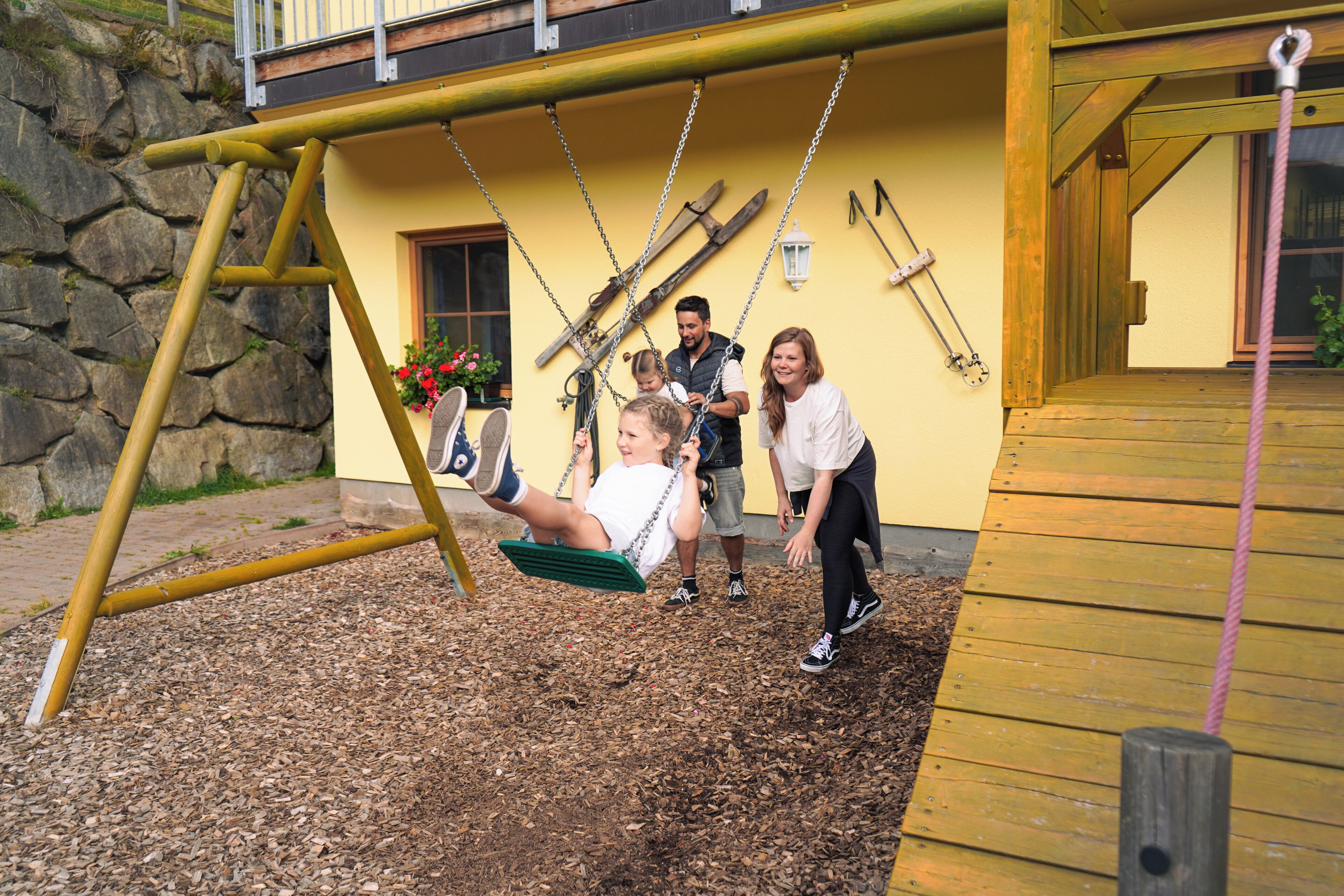 A wooden swing set with metal chains, a stone wall, and a wooden deck.