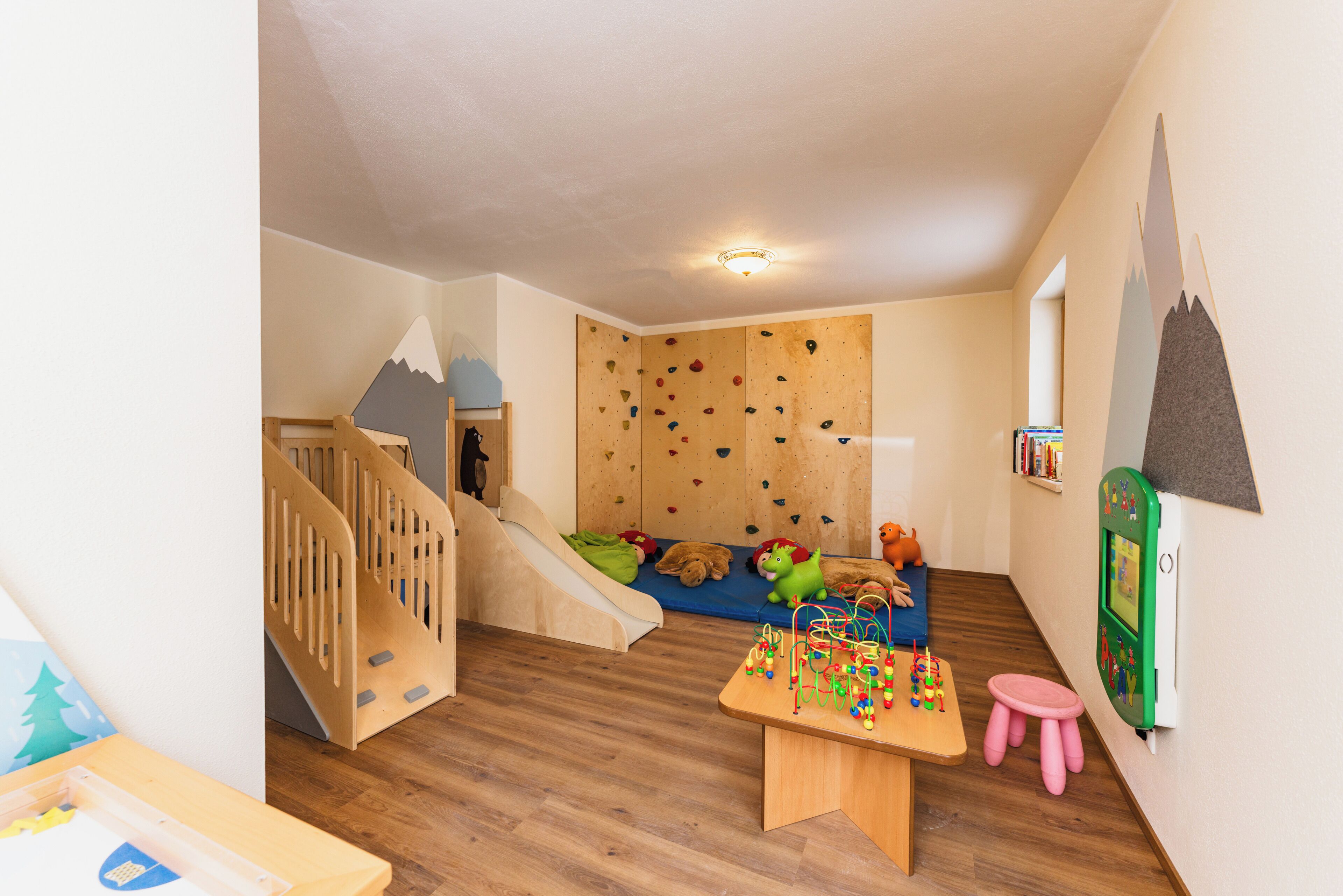 Un salón infantil con una pared de escalar, un tobogán y una mesa de juegos.