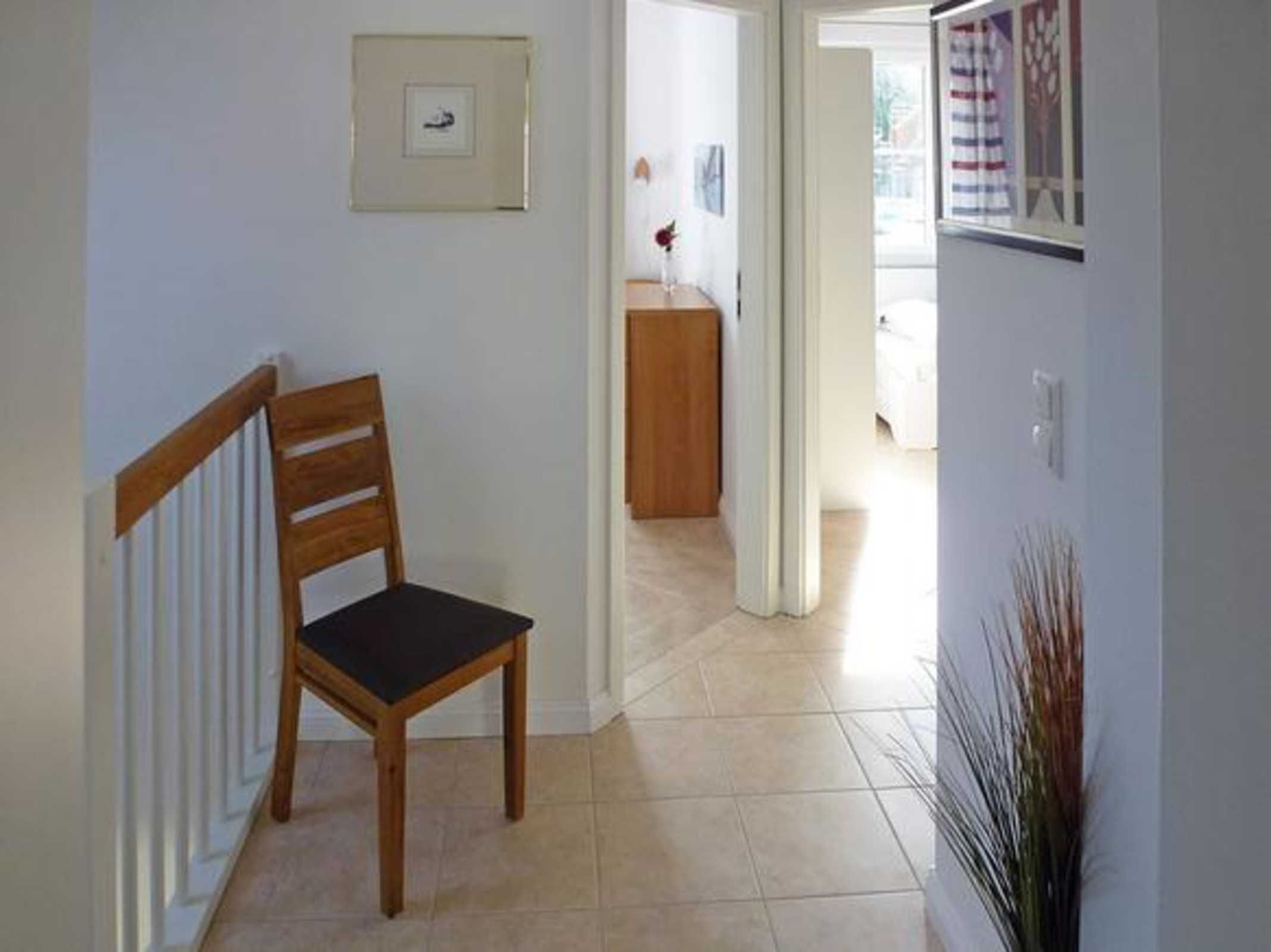 A hallway with a wooden chair, a radiator, a framed picture on the wall, and a plant.