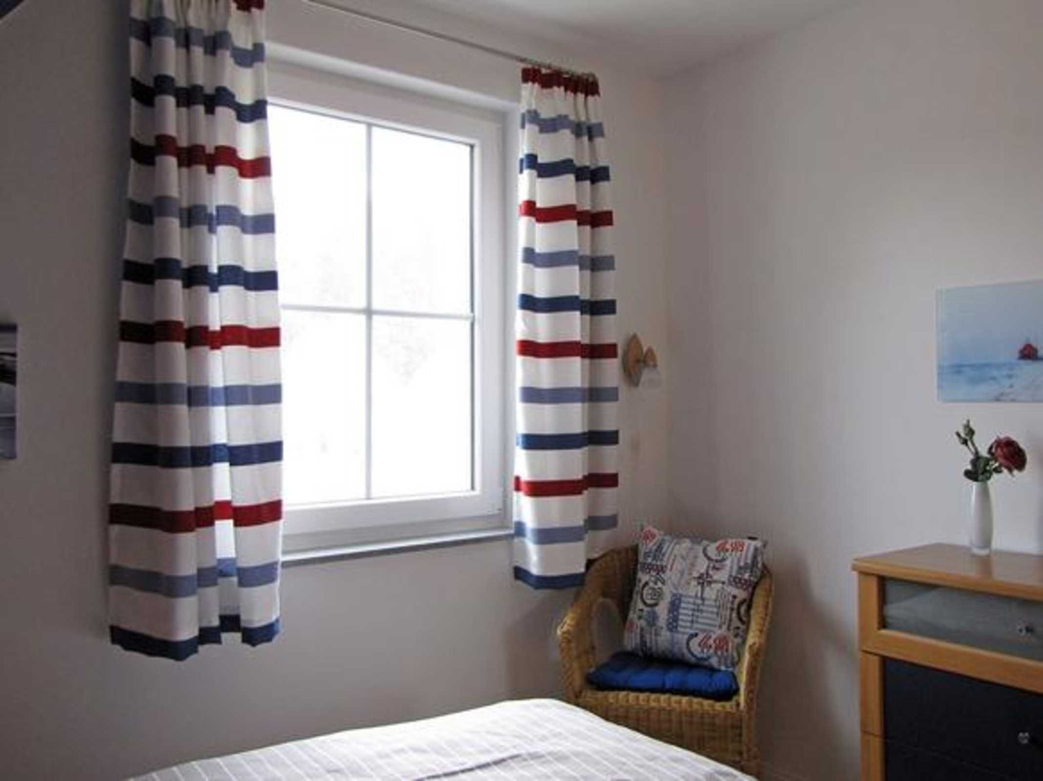 A bedroom with a bed, a chair with a cushion, a wooden nightstand, and curtains with a striped pattern.