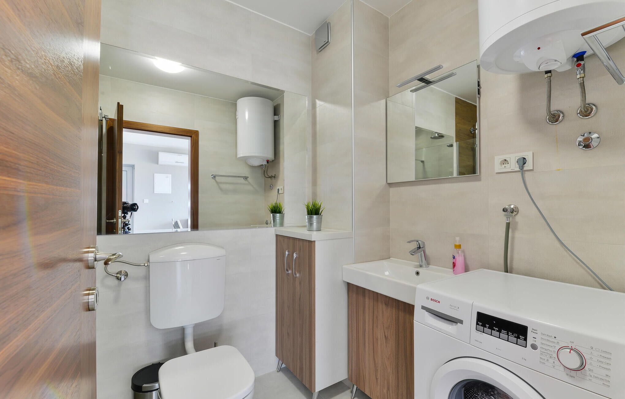 Une salle de bain moderne équipée de toilettes, d’un lavabo, d’un miroir et d’un lave-linge Bosch.