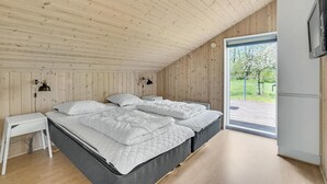 Een moderne slaapkamer met twee bedden, een klein nachtkastje, een televisie en een groot raam met uitzicht op groen.