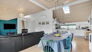Een moderne woonruimte met een leren zwarte bank, een eettafel met stoelen, een keuken en een aan de muur bevestigde televisie.