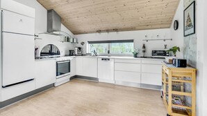 Een moderne keuken met witte kasten, een ingebouwde oven, een fornuis en een magnetron. Er is een houten plafond, een raam en een plant op het aanrecht.