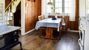 Une cuisine avec des murs en bois, une table à manger avec des chaises, un poêle et une fenêtre avec des rideaux.