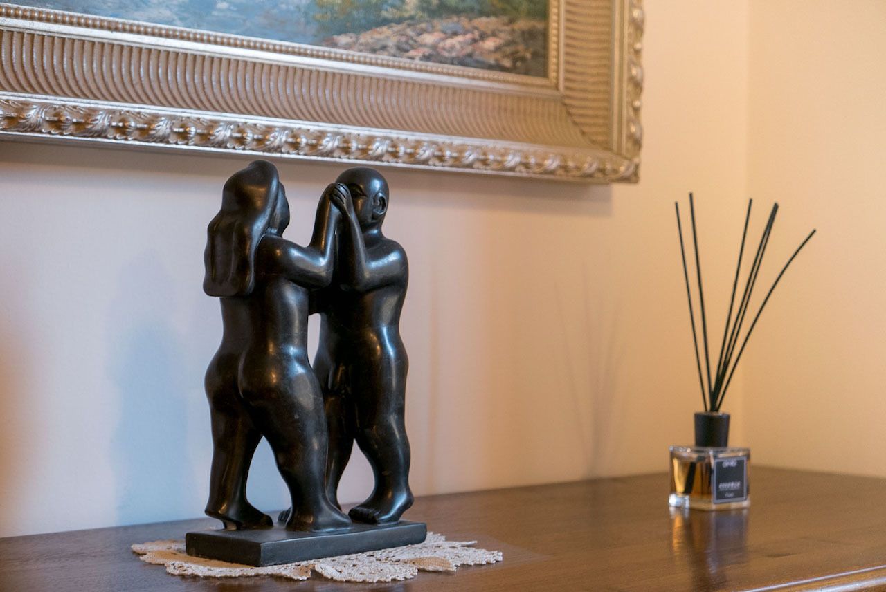A statue of two figures on a table with a decorative mirror and reed diffuser in the background.