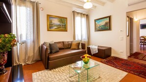 A living room with a brown leather sofa, a glass coffee table with a fruit bowl, a patterned rug, and two paintings on the wall. - Residenza Vescovado (Vicenza)