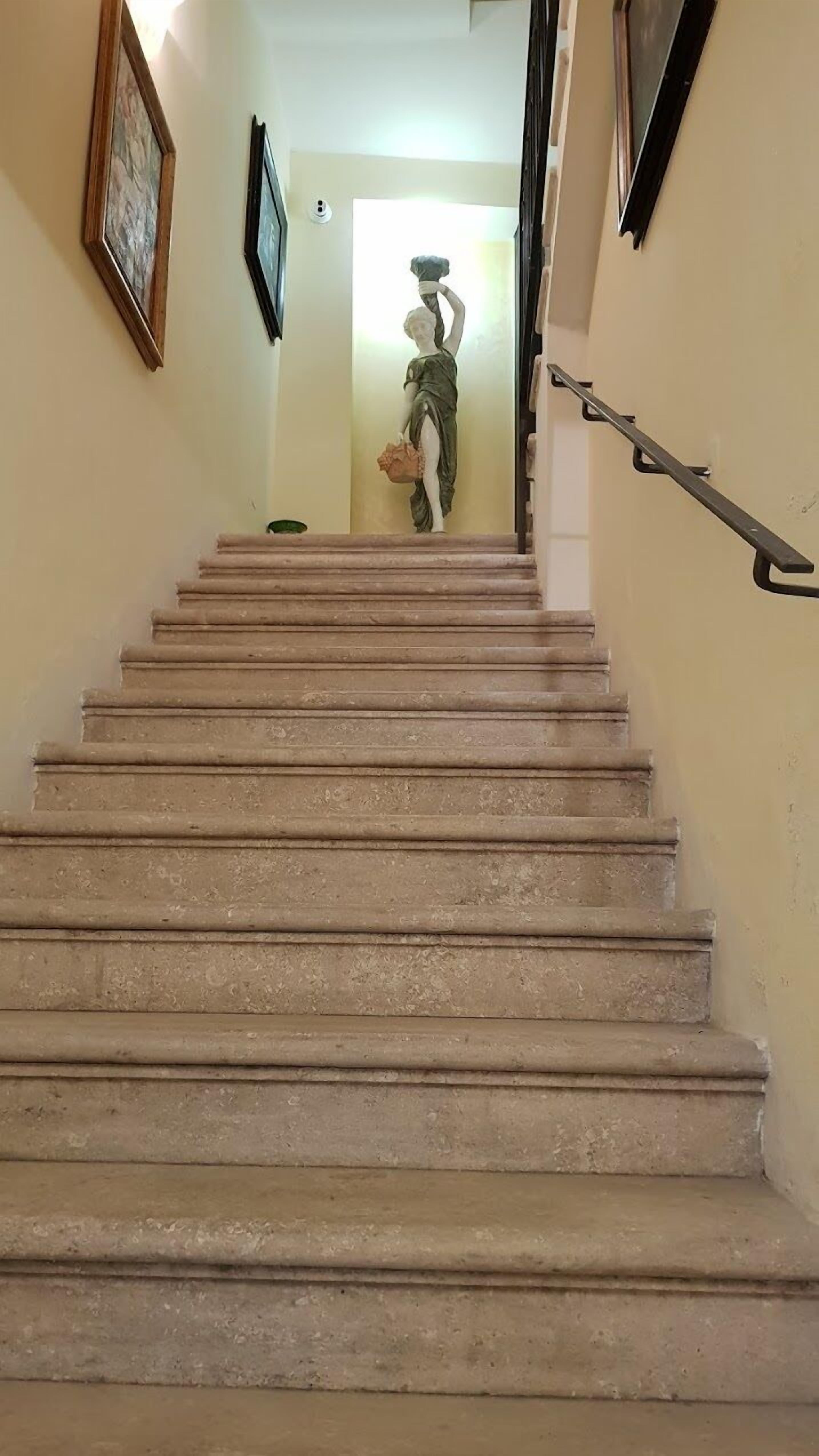 A staircase with a handrail, leading to a room with a statue.